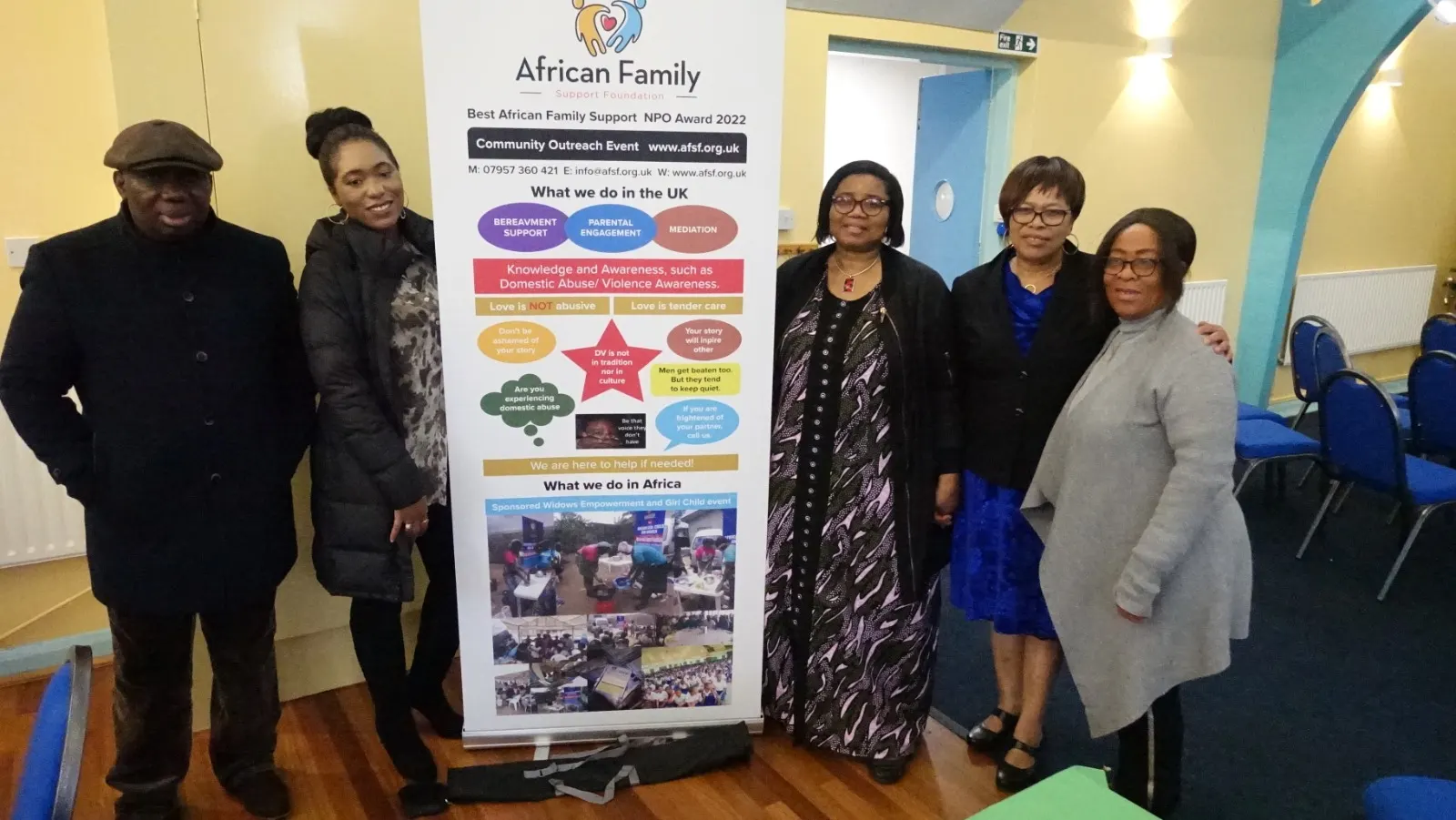 A large group photo of community members and staff standing behind an AFSF banner at an outdoor event.